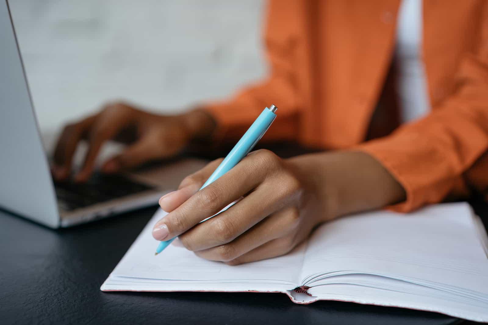 Close-up shot of student hand holding pen and writing in notebook, working at home. 电子学习